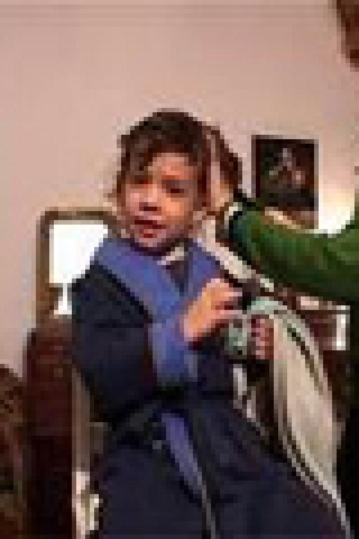 Ein Kind im Bademantel sitzt, während eine Frau seine Haare kämmt.