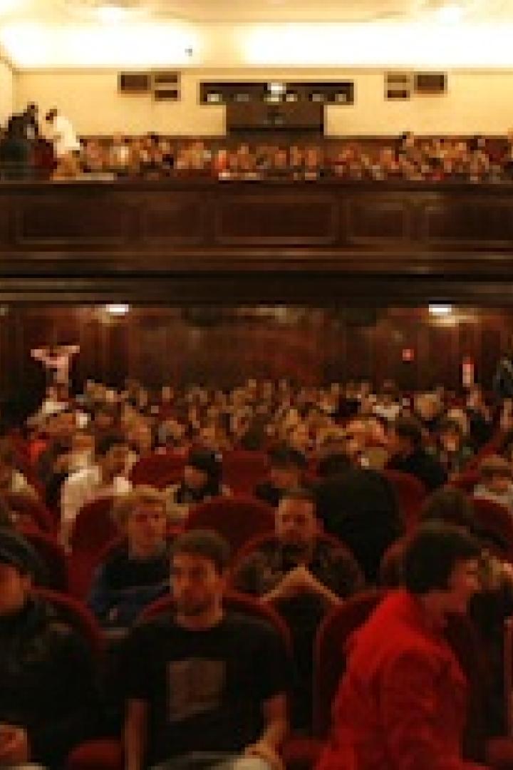 Ein volles Theater mit Zuschauern auf den Sitzen und auf dem Balkon.