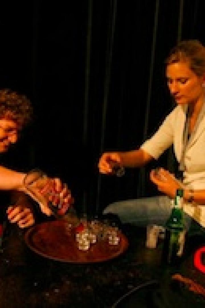 Ein Mann und eine Frau sitzen an einem Tisch und schenken Getränke in Schnapsgläser ein.