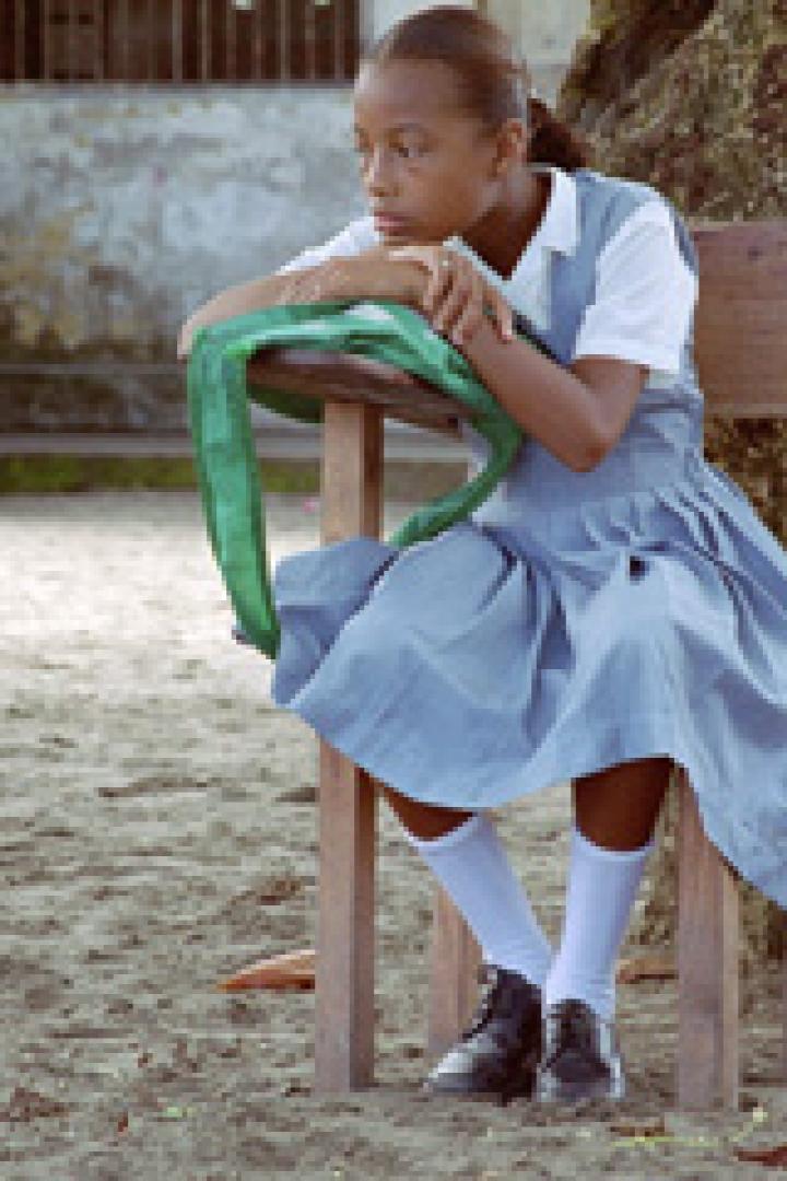 Ein junges Mädchen in Schuluniform sitzt auf einem Stuhl und blickt nachdenklich zur Seite.