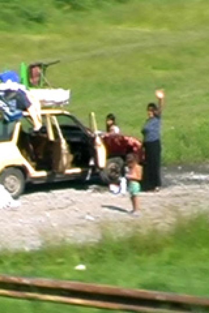 Eine Familie steht neben einem vollgepackten Auto am Straßenrand.