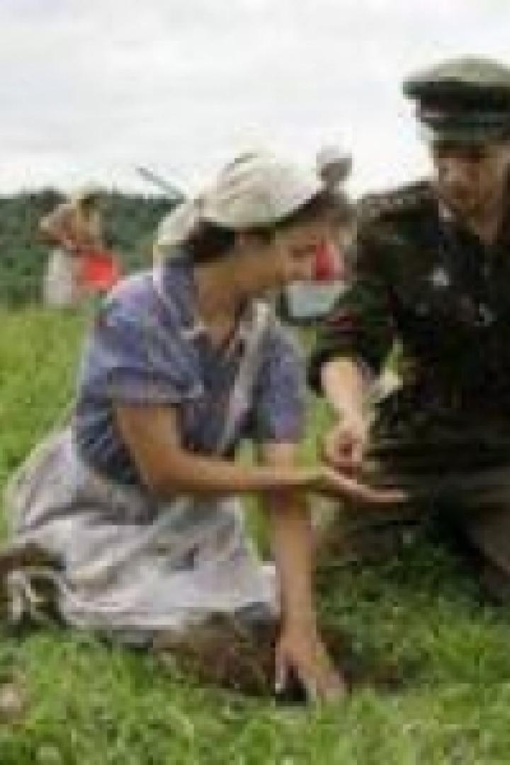 Eine Frau im Kleid und ein Soldat knien auf einem Feld.