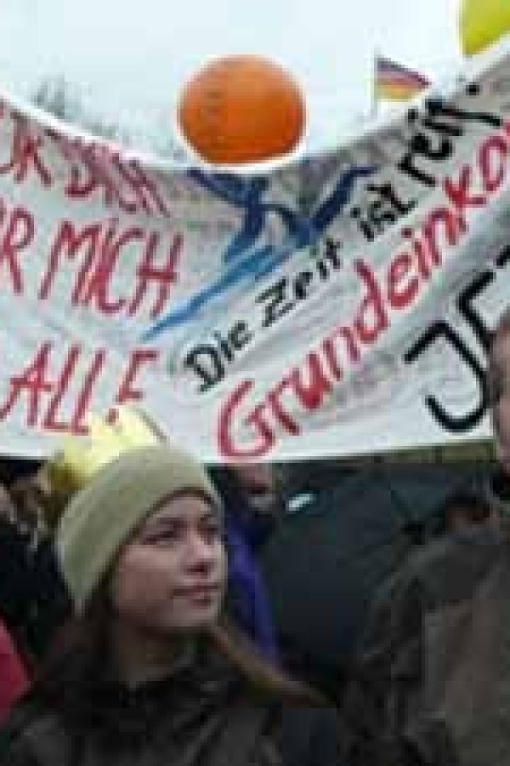 Menschen demonstrieren für ein Grundeinkommen, mit einem Banner „Für dich, für mich, für alle“.