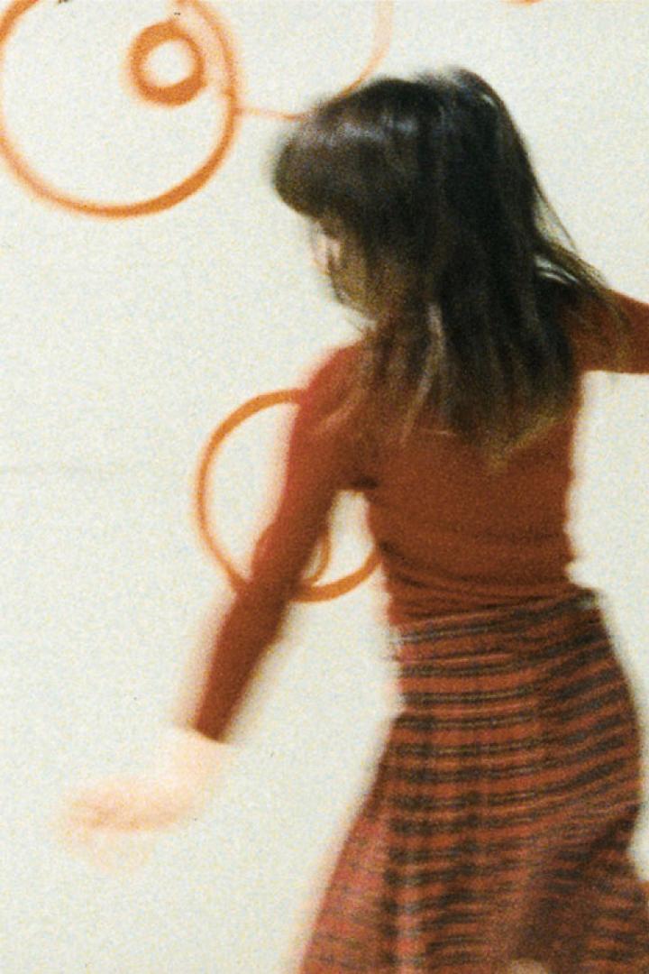 Ein Mädchen tanzt vor einer Wand mit orangefarbenen Kreisen.