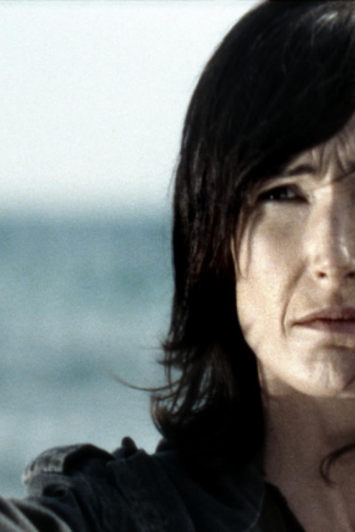 Eine Frau hält ein Glas Sekt vor dem Hintergrund des Meeres.