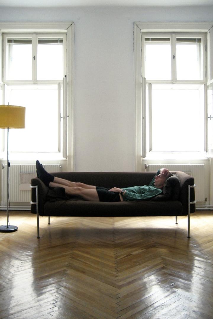 Ein Mann liegt entspannt auf einem Sofa in einem hellen Raum.
