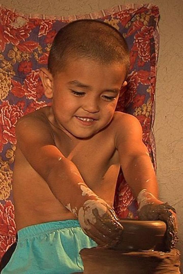 Ein Junge formt mit schmutzigen Händen einen Tontopf.