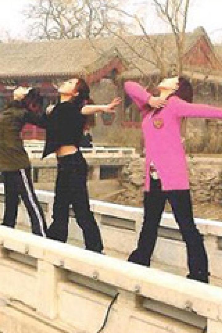Eine Gruppe junger Frauen posiert auf einer Brücke mit einem traditionellen chinesischen Gebäude im Hintergrund.