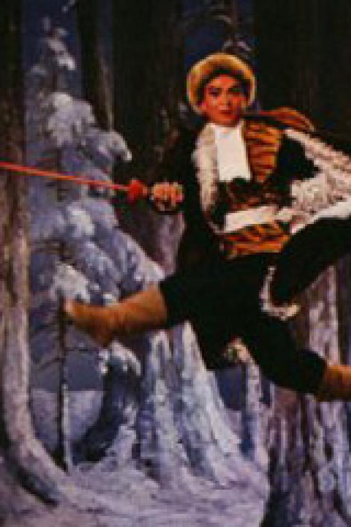 Ein Tänzer in einem Kostüm springt vor einem Bühnenbild mit verschneiten Bäumen.