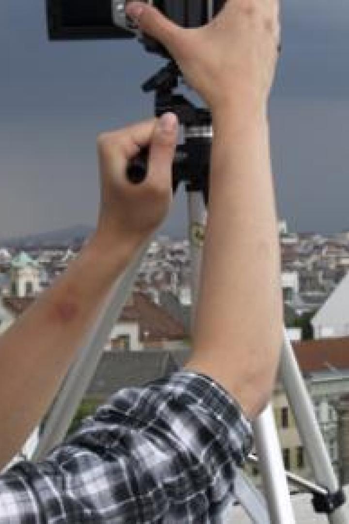 Eine Person fotografiert mit einem Stativ eine Stadtansicht unter einem bewölkten Himmel.