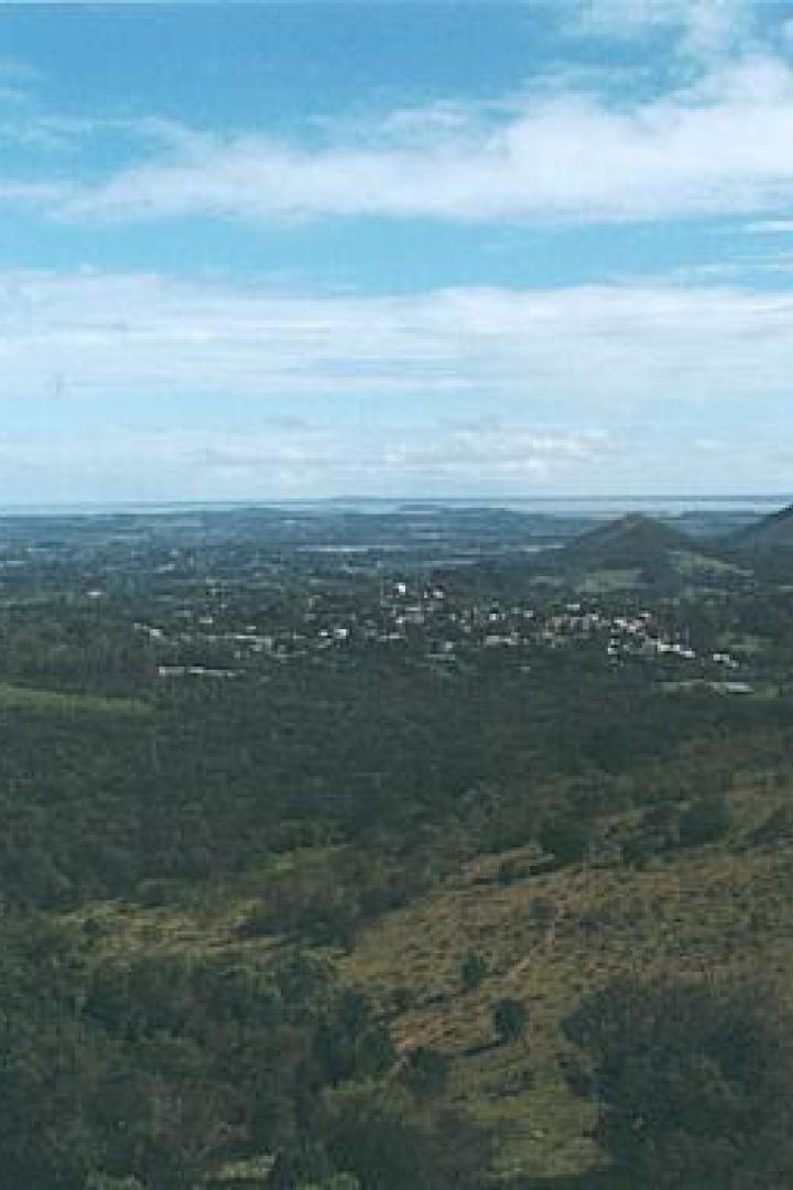 Eine weite Landschaft mit Hügeln, Wäldern und einer Stadt unter blauem Himmel.