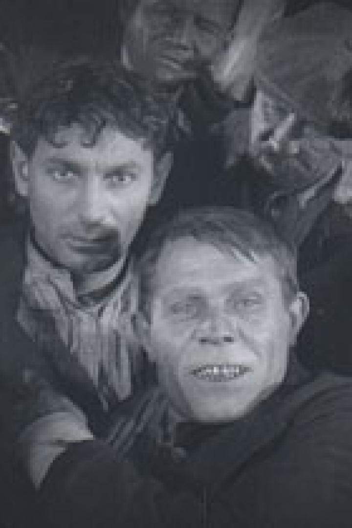 Eine Gruppe von Männern, einige mit besorgten Gesichtsausdrücken, in einer dunklen Umgebung.