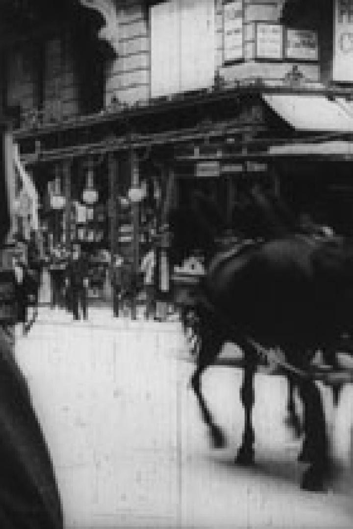 Eine belebte Straße mit einer Pferdekutsche und Passanten in einer historischen Aufnahme.
