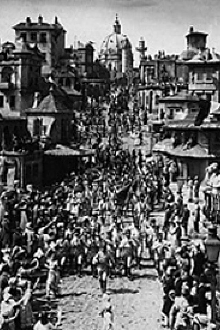 Eine Menschenmenge marschiert eine Straße in einer Stadt hinauf, im Hintergrund eine Kuppel.