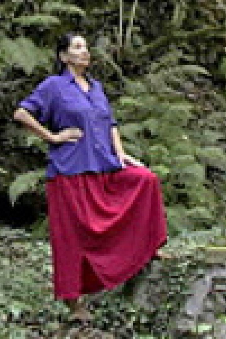 Eine Frau in einem blauen Hemd und einem roten Rock posiert in einem Wald.