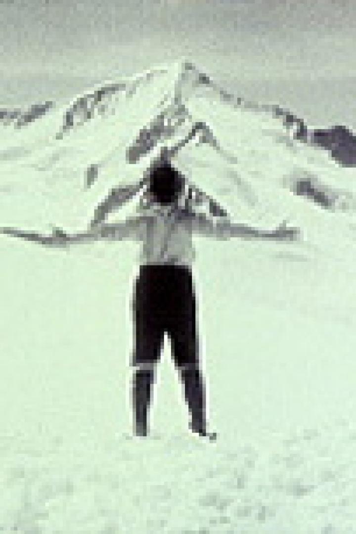 Eine Person steht mit ausgestreckten Armen vor einem schneebedeckten Berg.