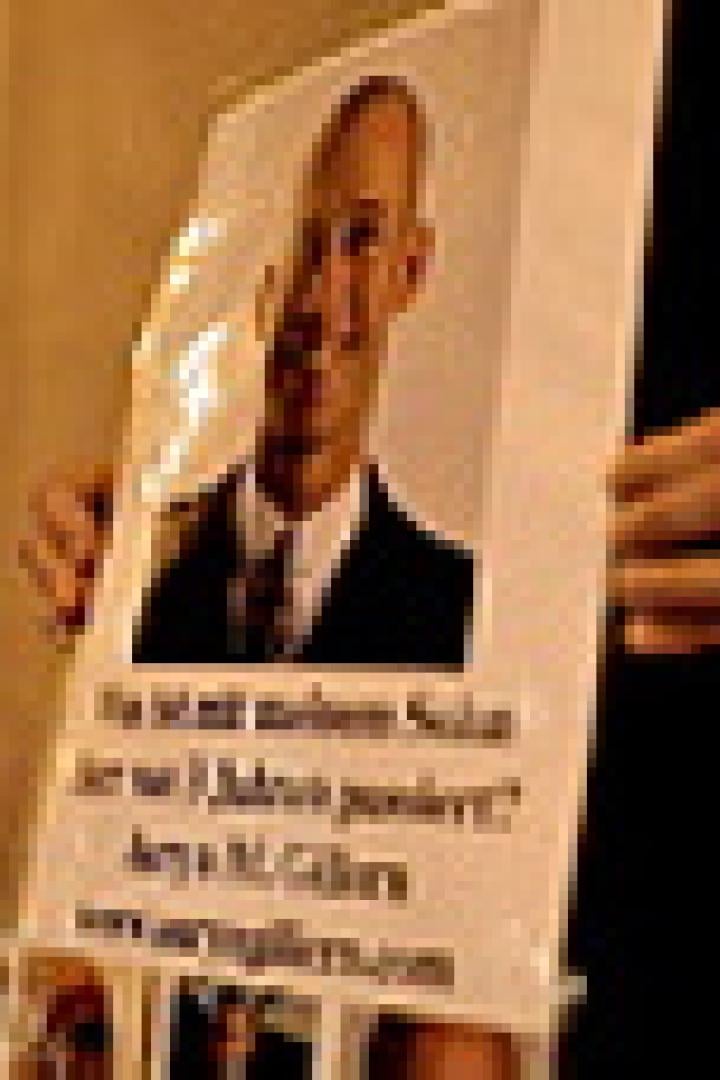 Eine Person hält ein Plakat mit dem Porträt von Aeya M. Gillers hoch.