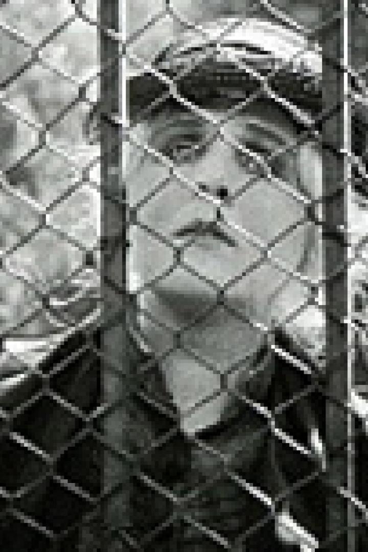 Eine Frau mit Mütze blickt durch einen Maschendrahtzaun nach oben.