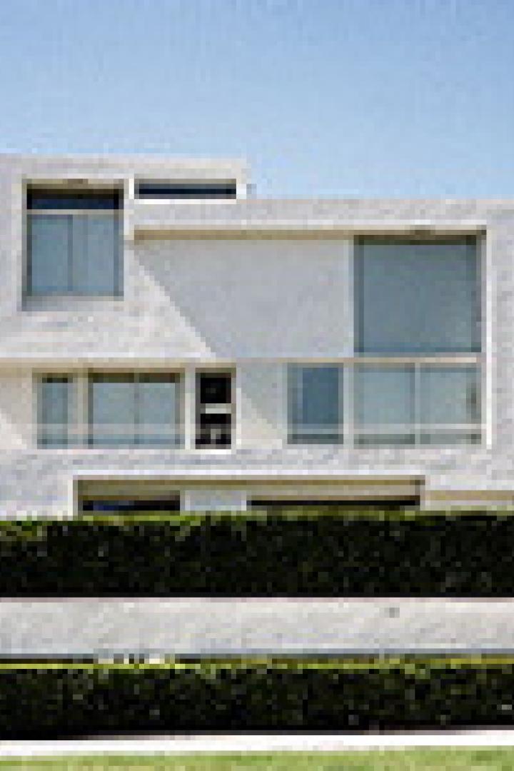 Ein modernes, weißes Haus mit großen Fenstern und einer grünen Hecke im Vorgarten.