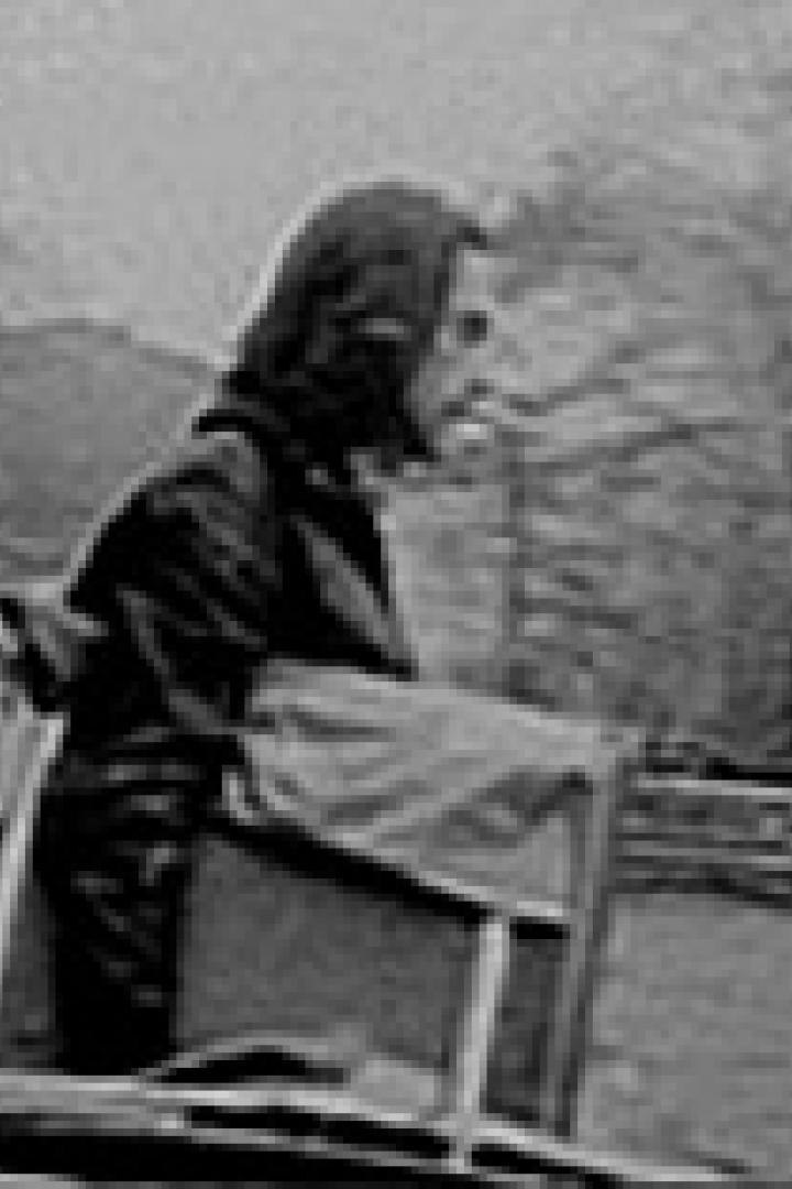 Eine Person mit Kapuze steht neben einem hölzernen Karren im Freien.