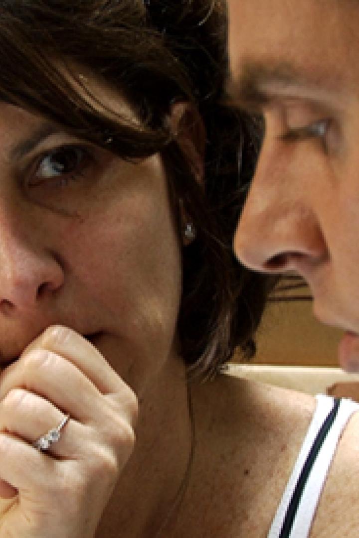 Eine Frau mit einem Ring am Finger wirkt besorgt, während ein Mann neben ihr aufmerksam zuhört.