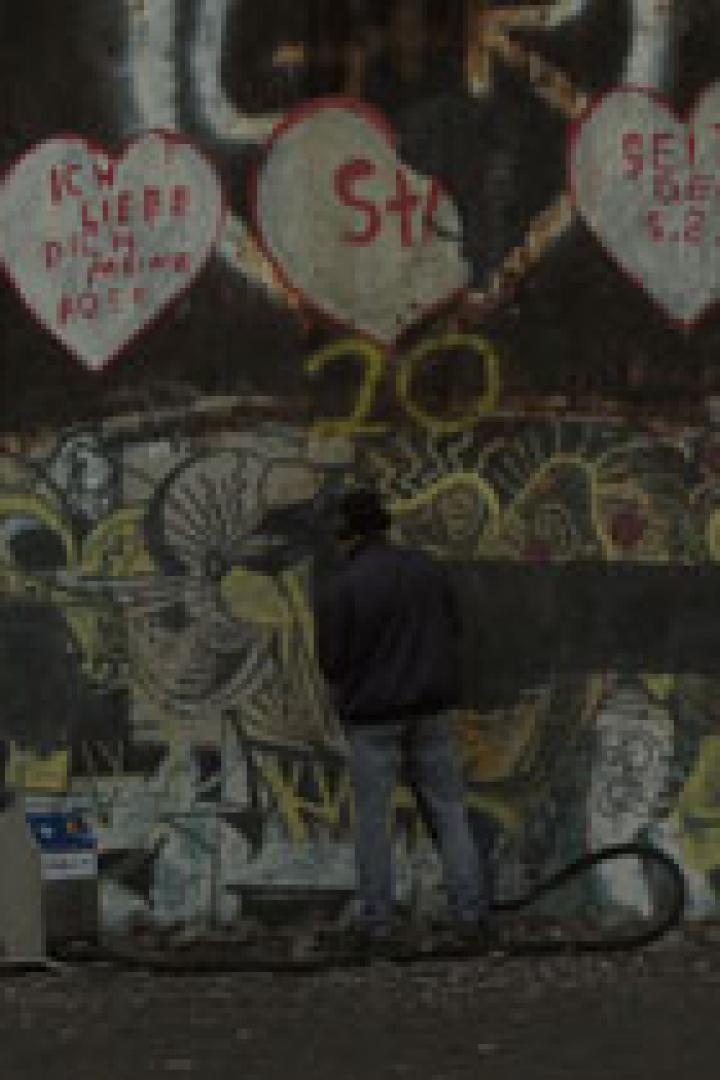 Eine Person reinigt Graffiti von einem Teil der Berliner Mauer.