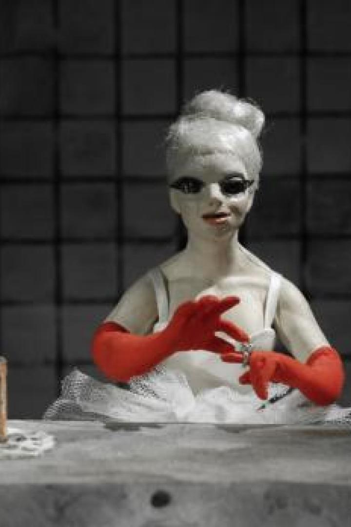 Eine Puppe mit roten Handschuhen und weißem Tutu sitzt an einem Tisch.