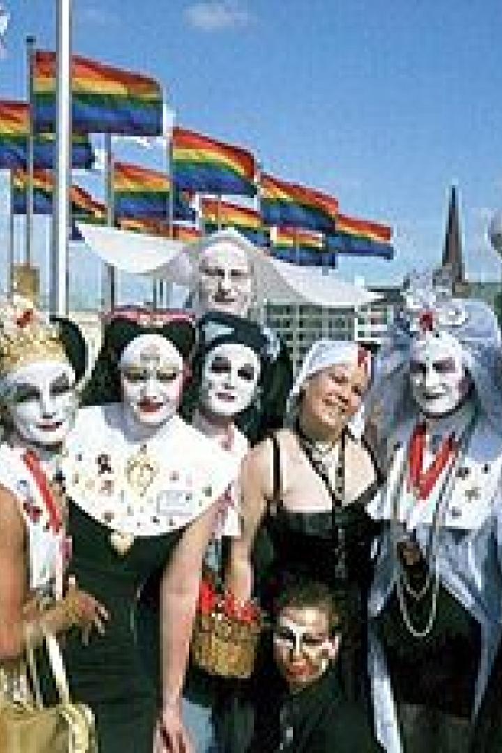 Eine Gruppe von Menschen, einige als Nonnen verkleidet, posiert vor Regenbogenflaggen.