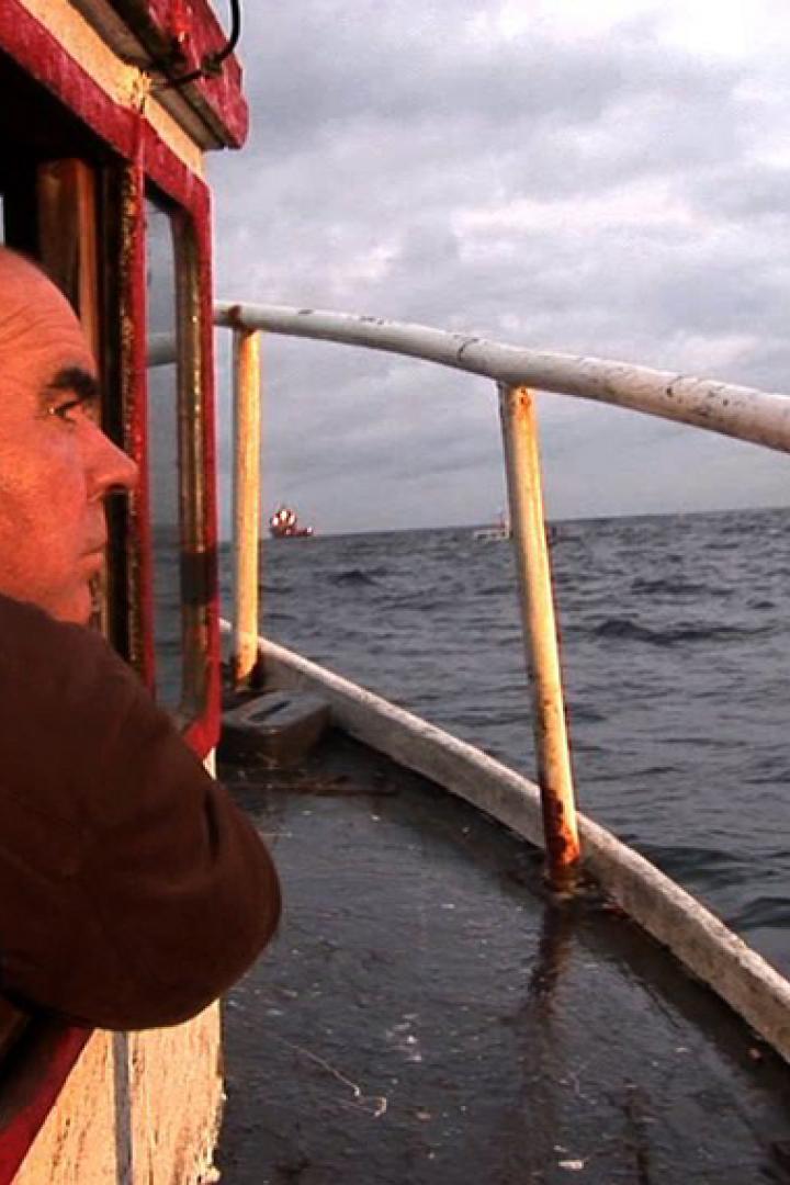 Ein Mann blickt von einem kleinen Boot auf ein großes Schiff auf dem Meer.