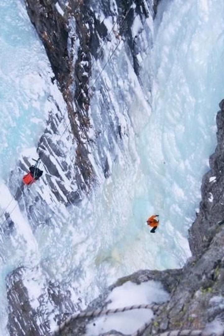 Zwei Personen überqueren eine eisige Schlucht mit einer Seilrutsche.
