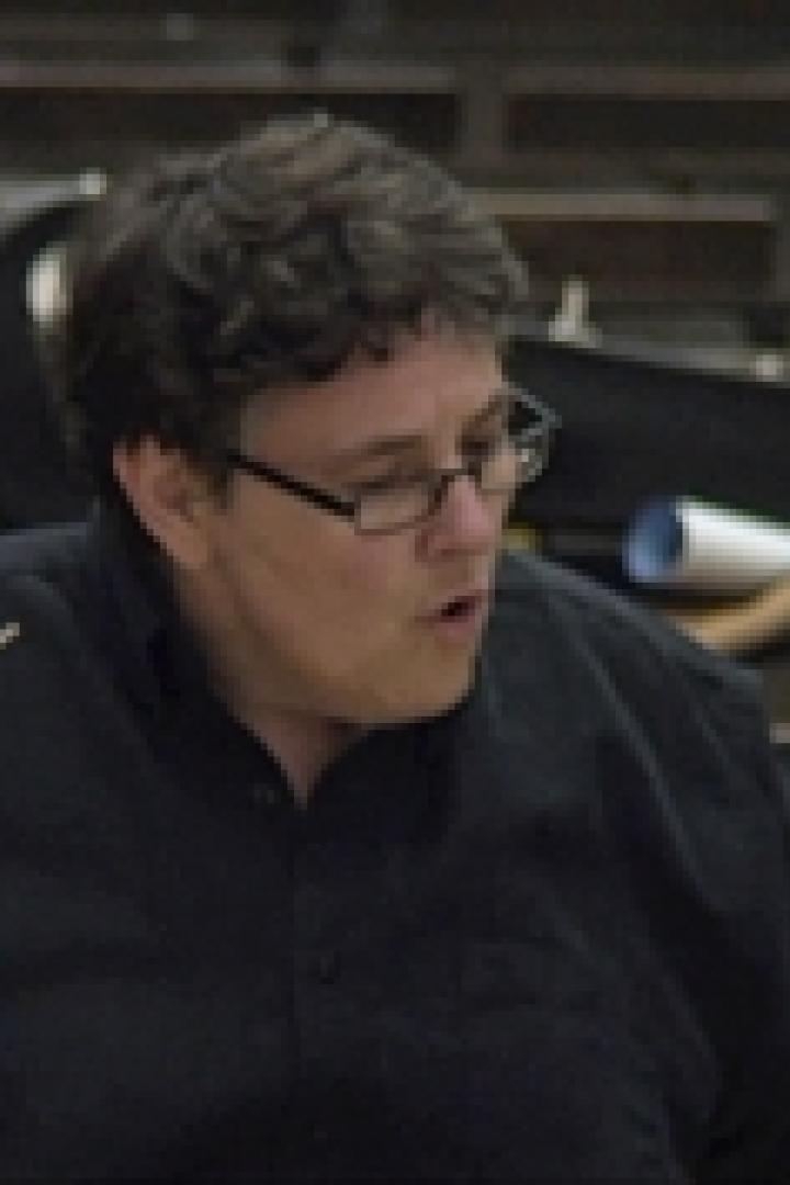 Ein Dirigent mit Brille dirigiert ein Orchester.