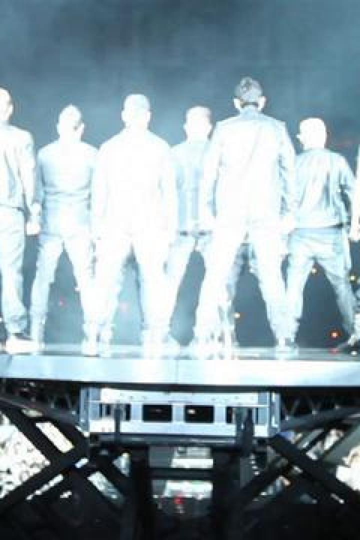 Eine Boyband steht auf einer Bühne vor einem großen Publikum.