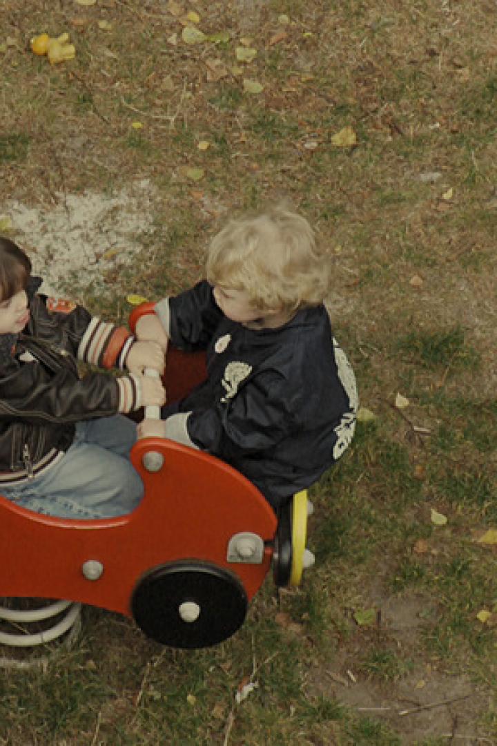 Zwei Kinder spielen auf einem roten Schaukeltier in Form eines Autos.
