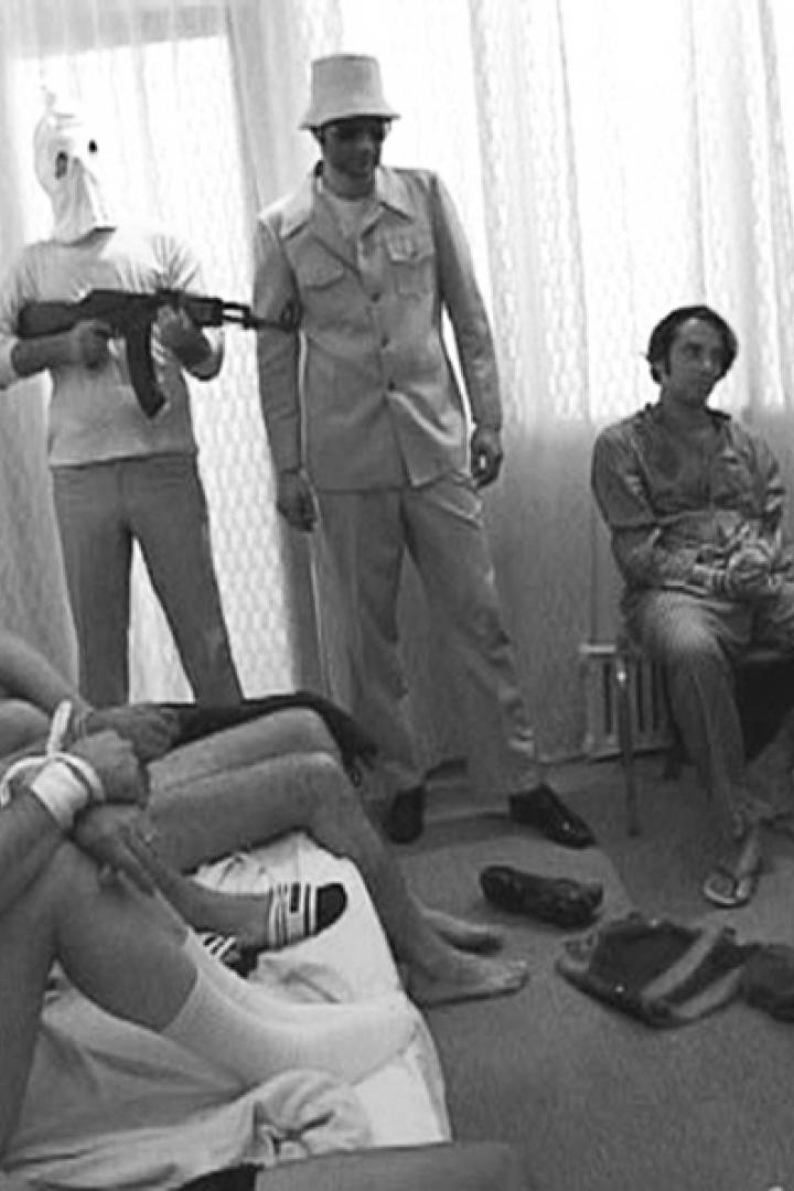 Geiseln sind gefesselt, während Bewaffnete in einem Raum stehen.