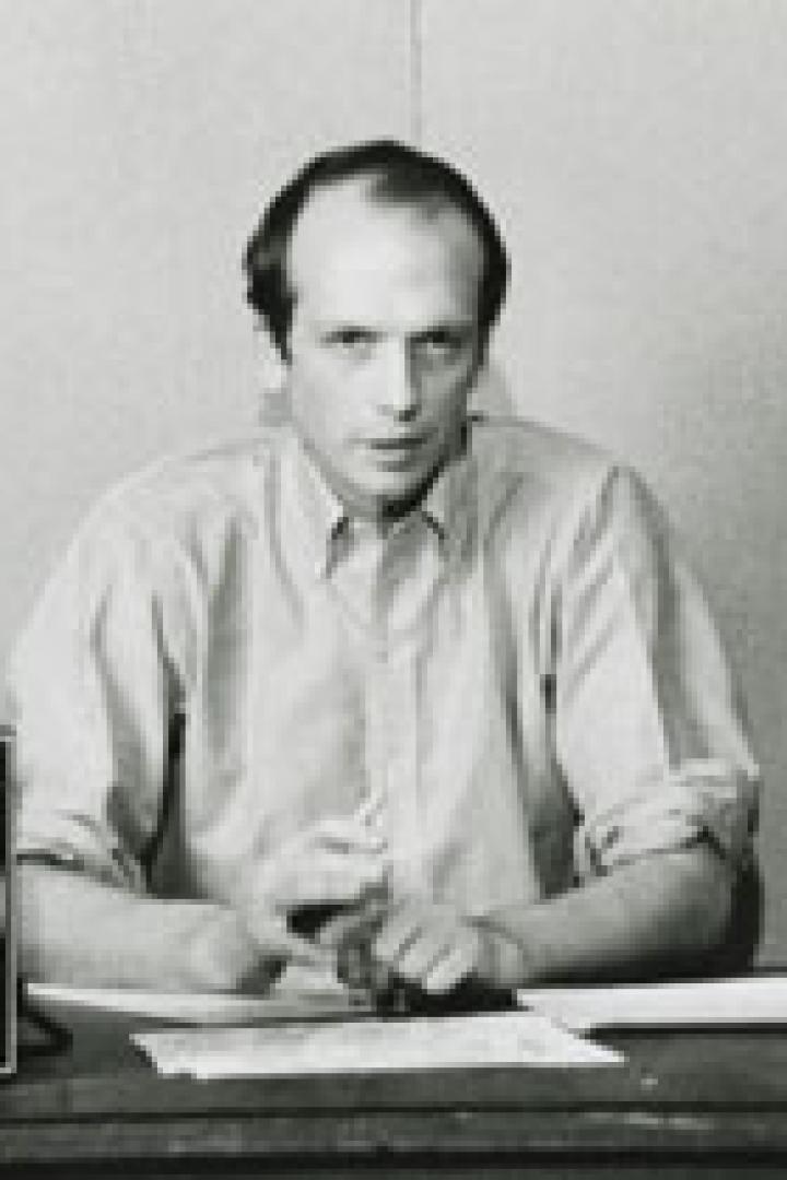 Ein Mann sitzt an einem Tisch mit einer großen Uhr und Papieren.