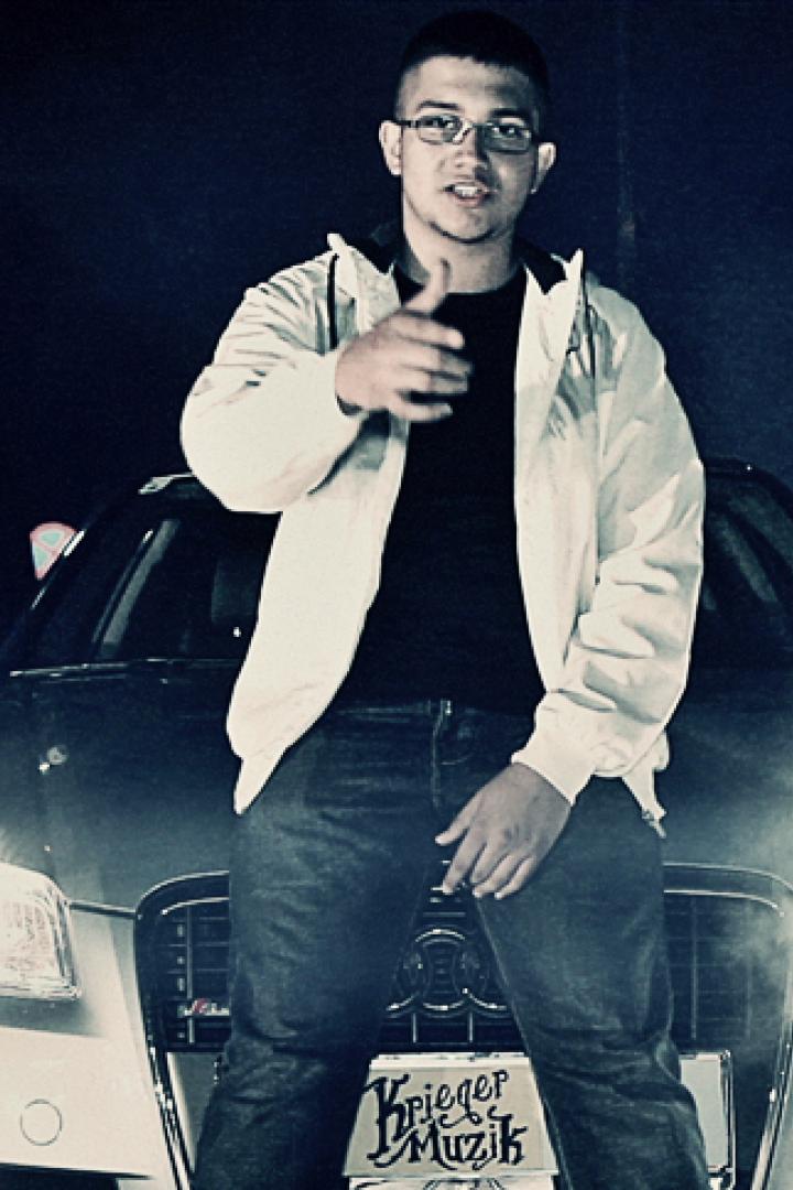 Ein junger Mann posiert vor einem Auto, flankiert von zwei Personen mit Masken.