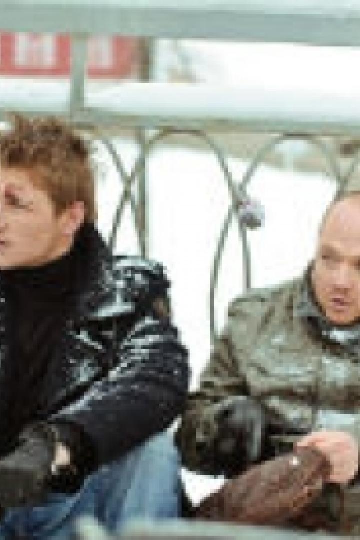 Zwei Männer sitzen im Winter auf einer Brücke mit Liebesschlössern.