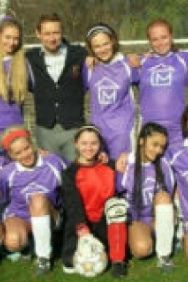 Eine Mädchenfußballmannschaft posiert mit ihrem Trainer für ein Gruppenfoto.