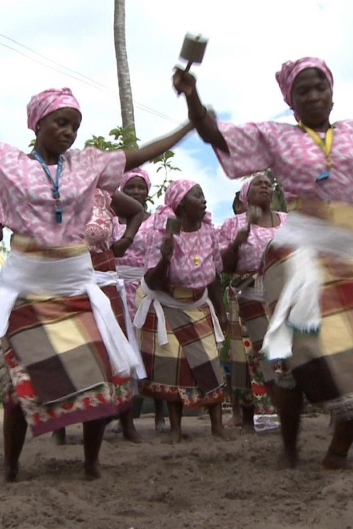 Eine Gruppe Frauen in traditioneller Kleidung tanzt am Strand.