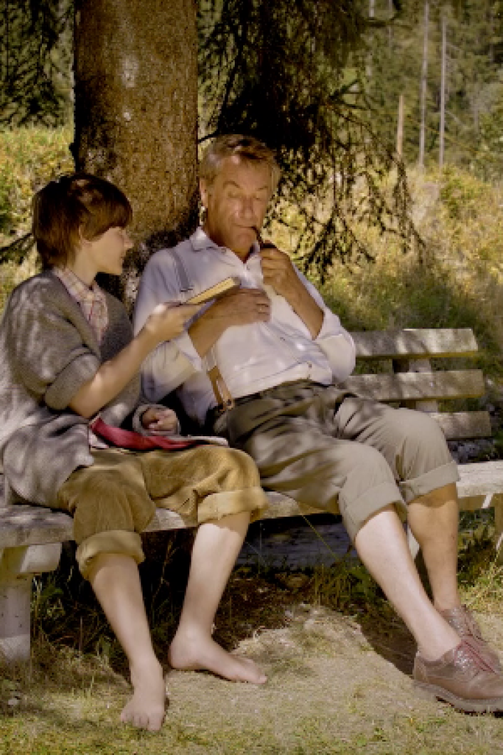 Ein Junge und ein älterer Mann sitzen barfuß auf einer Bank im Grünen.
