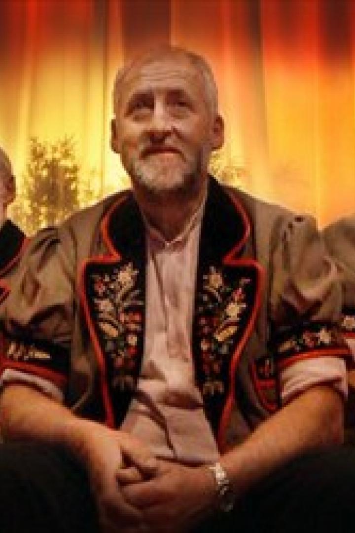 Drei ältere Männer in Trachten sitzen nebeneinander vor einem Vorhang.