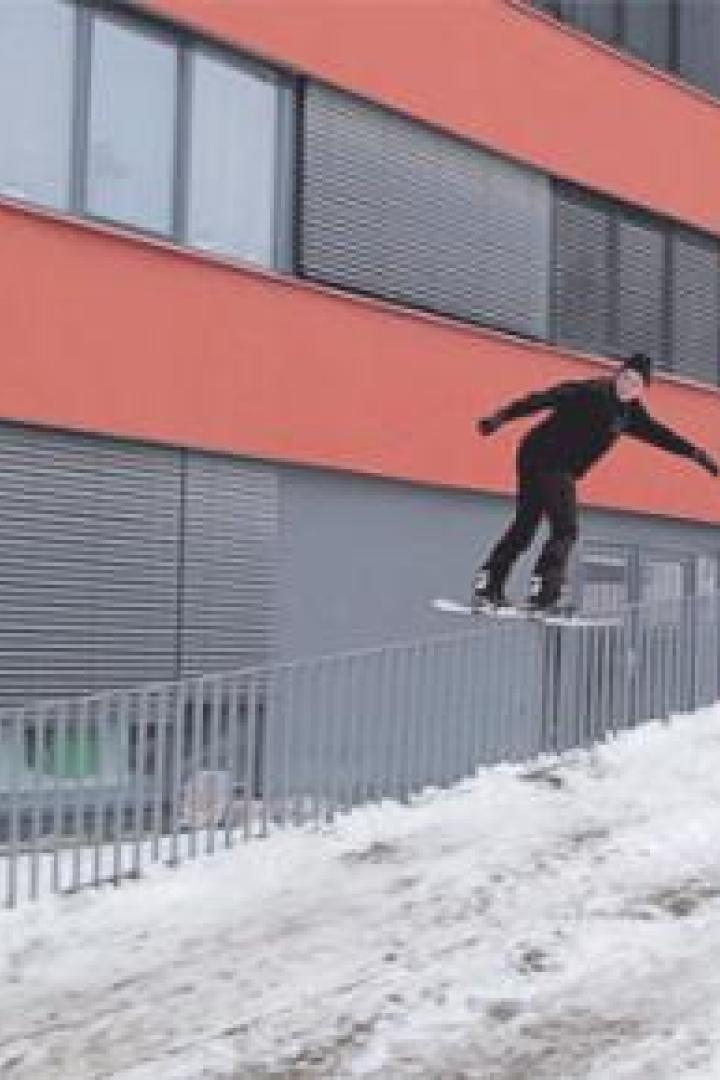 Ein Snowboarder springt über eine Rampe vor einem orangefarbenen Gebäude.