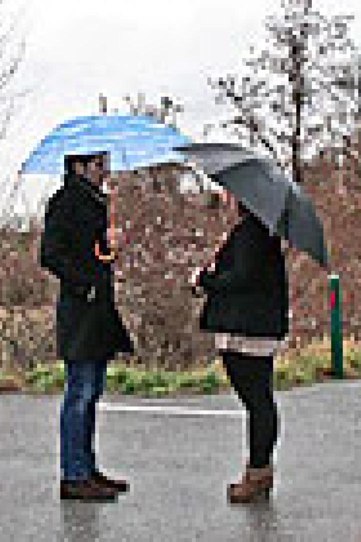 Zwei Personen stehen mit Regenschirmen im Regen und unterhalten sich.