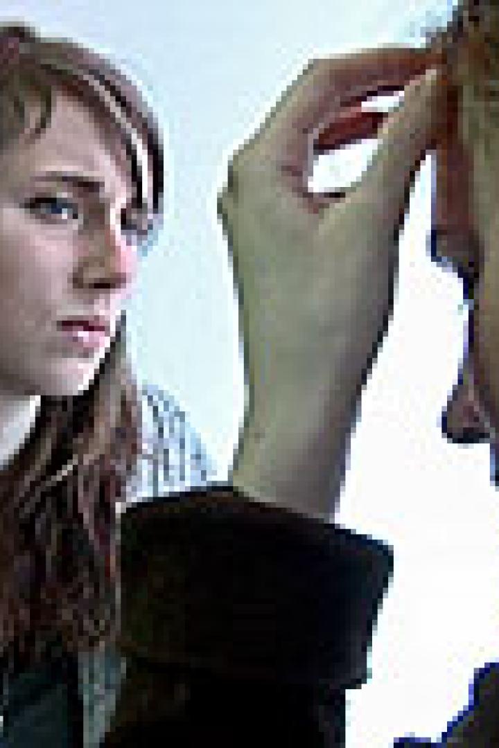 Zwei Frauen sitzen an einem Tisch, eine wirkt besorgt, die andere hält ihre Hand an die Stirn.