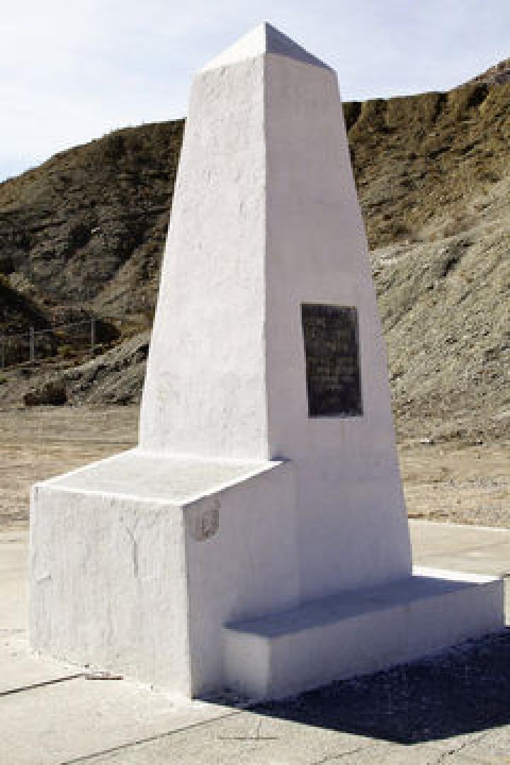 Ein weißes Denkmal steht vor einer kargen Hügellandschaft.