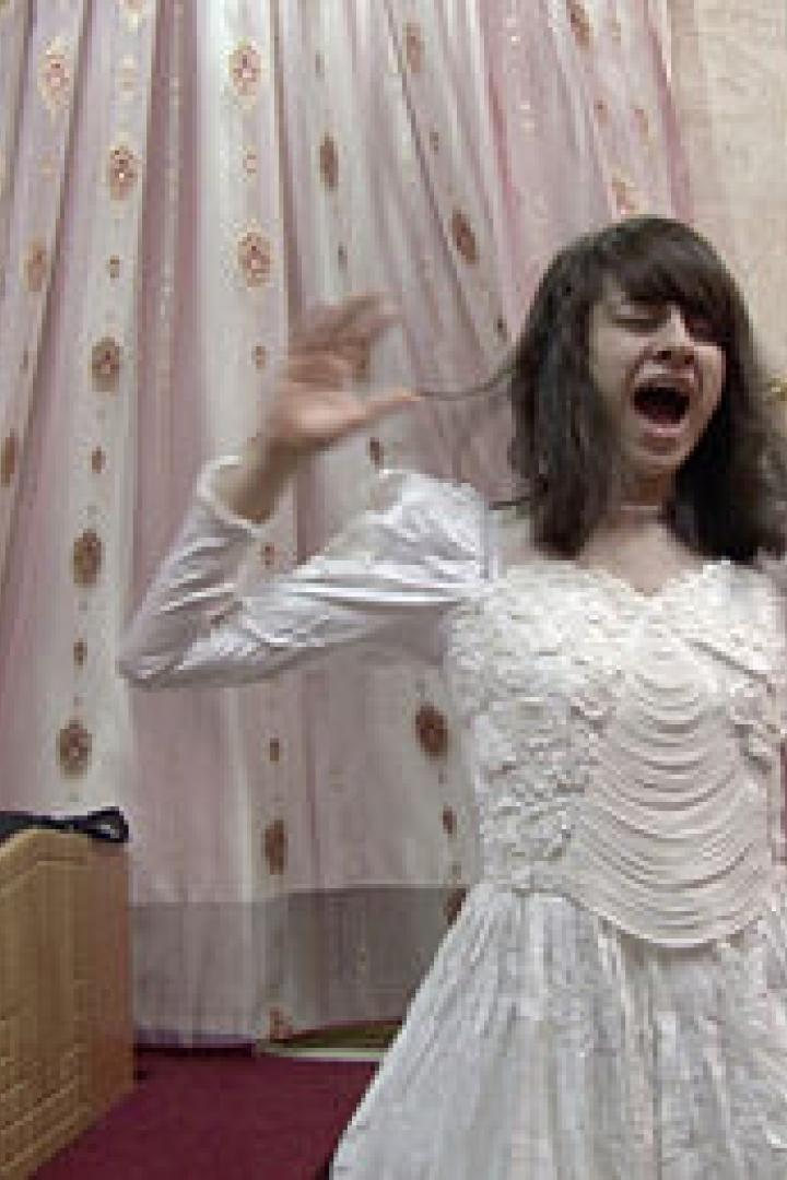 Eine junge Frau im Hochzeitskleid schreit mit erhobenen Händen.