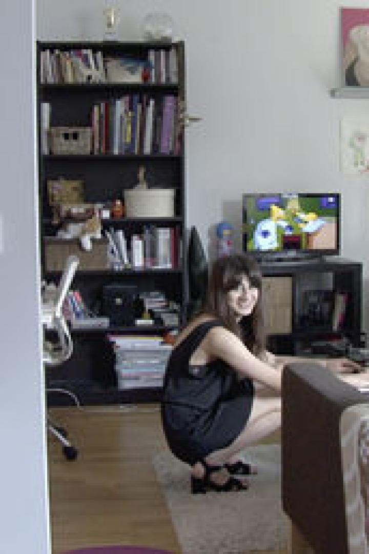 Eine Frau hockt in einem Wohnzimmer und benutzt einen Laptop.