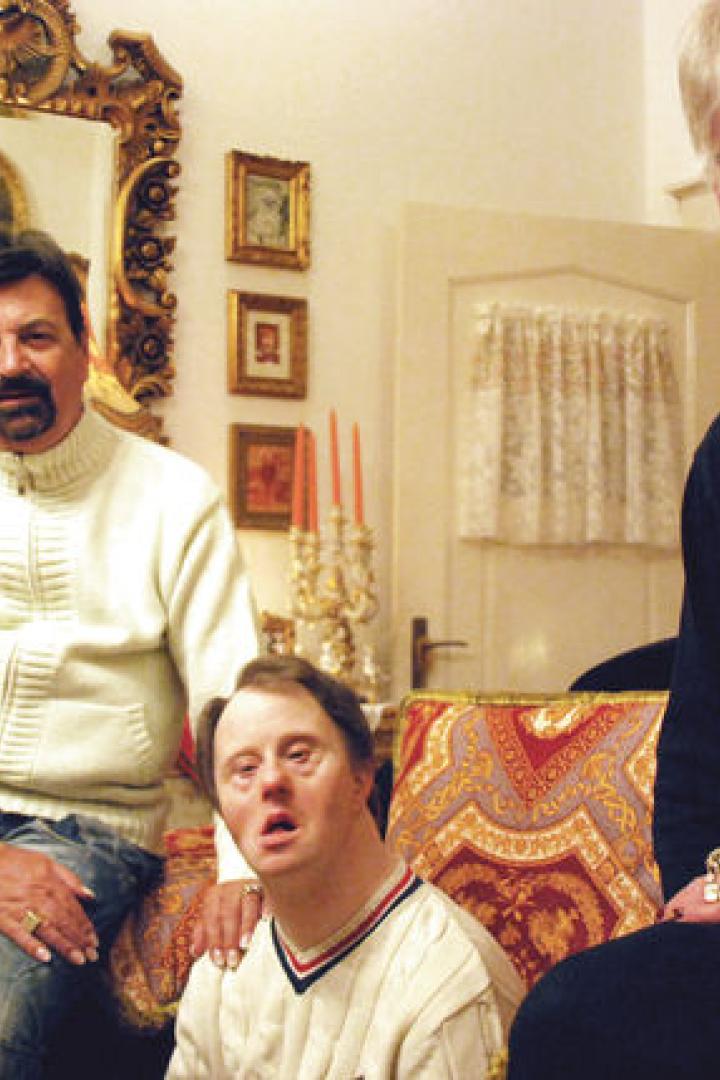 Drei Personen sitzen in einem reich verzierten Wohnzimmer.