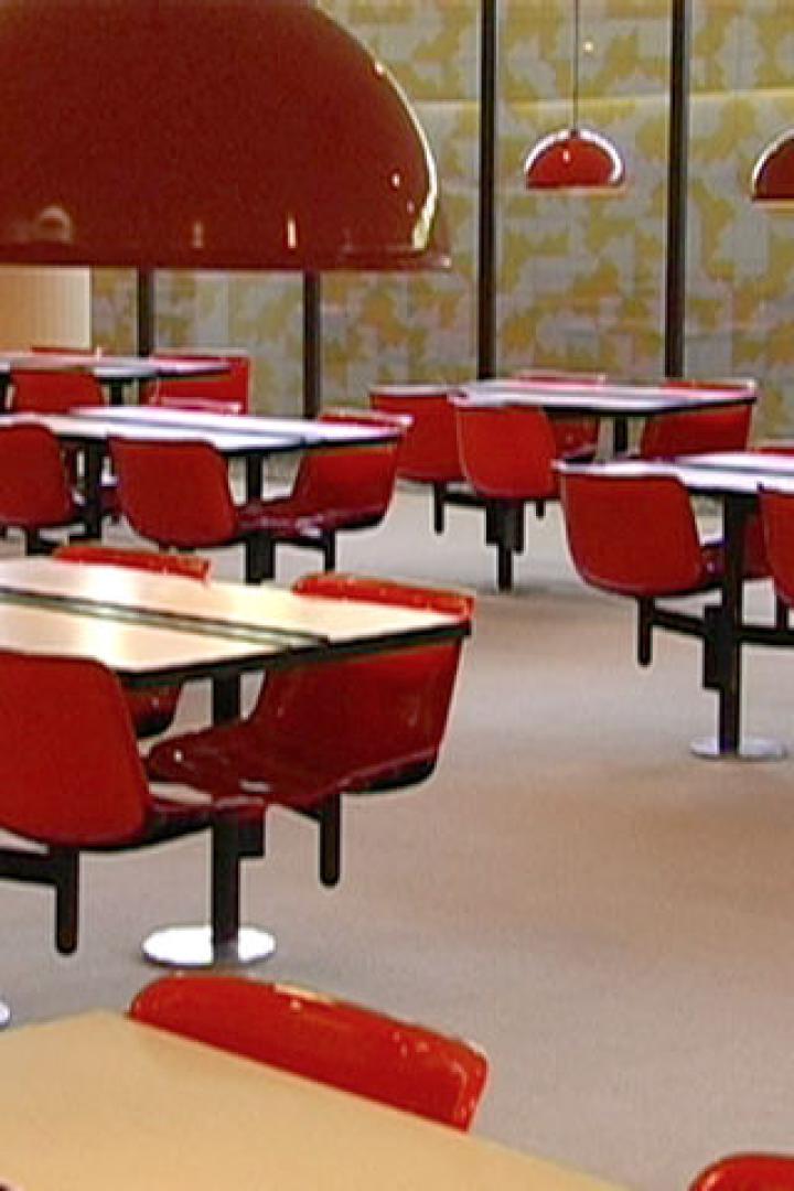 Ein Speisesaal mit roten Stühlen und Tischen unter großen, roten Lampen.