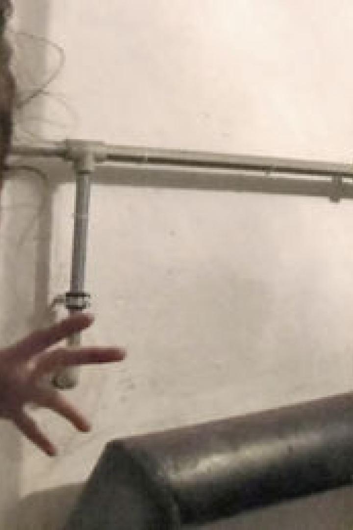 Eine junge Frau steht vor einer Wand mit Rohren und einem Zähler.